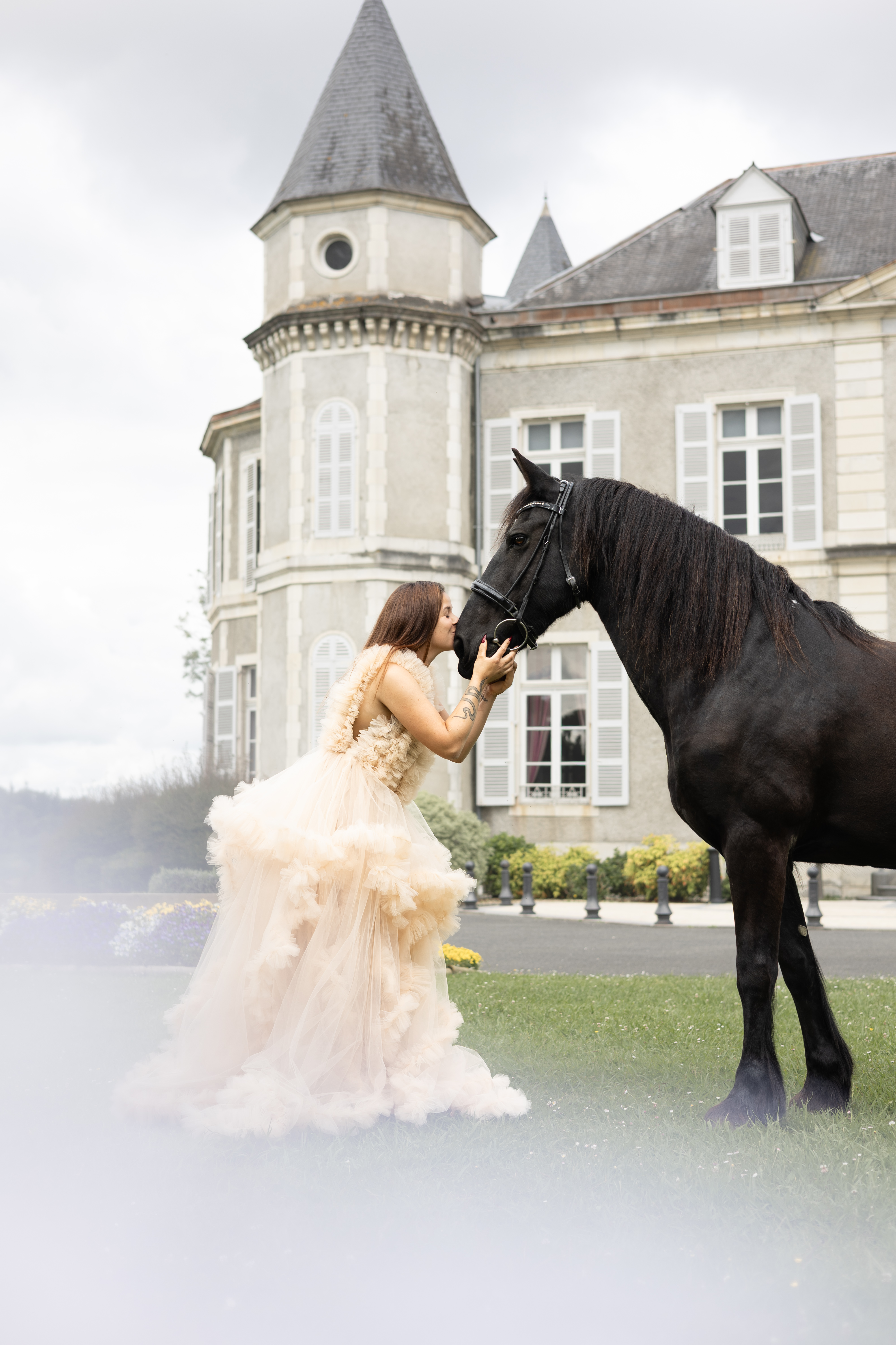 Femme en robe ivoire caressant un cheval noir devant un château
