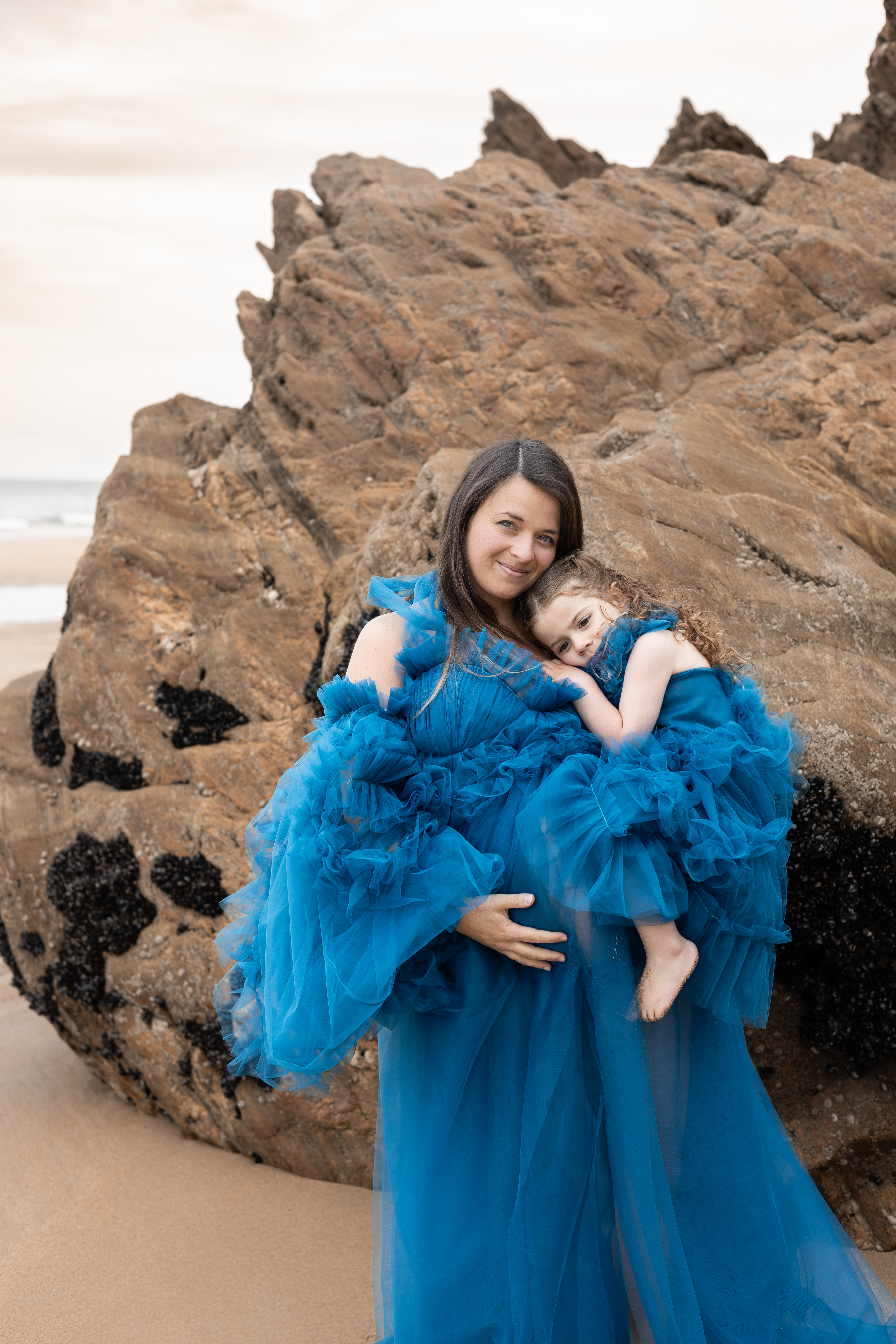 Mère en robe bleue portant sa petite fille devant de grands rochers