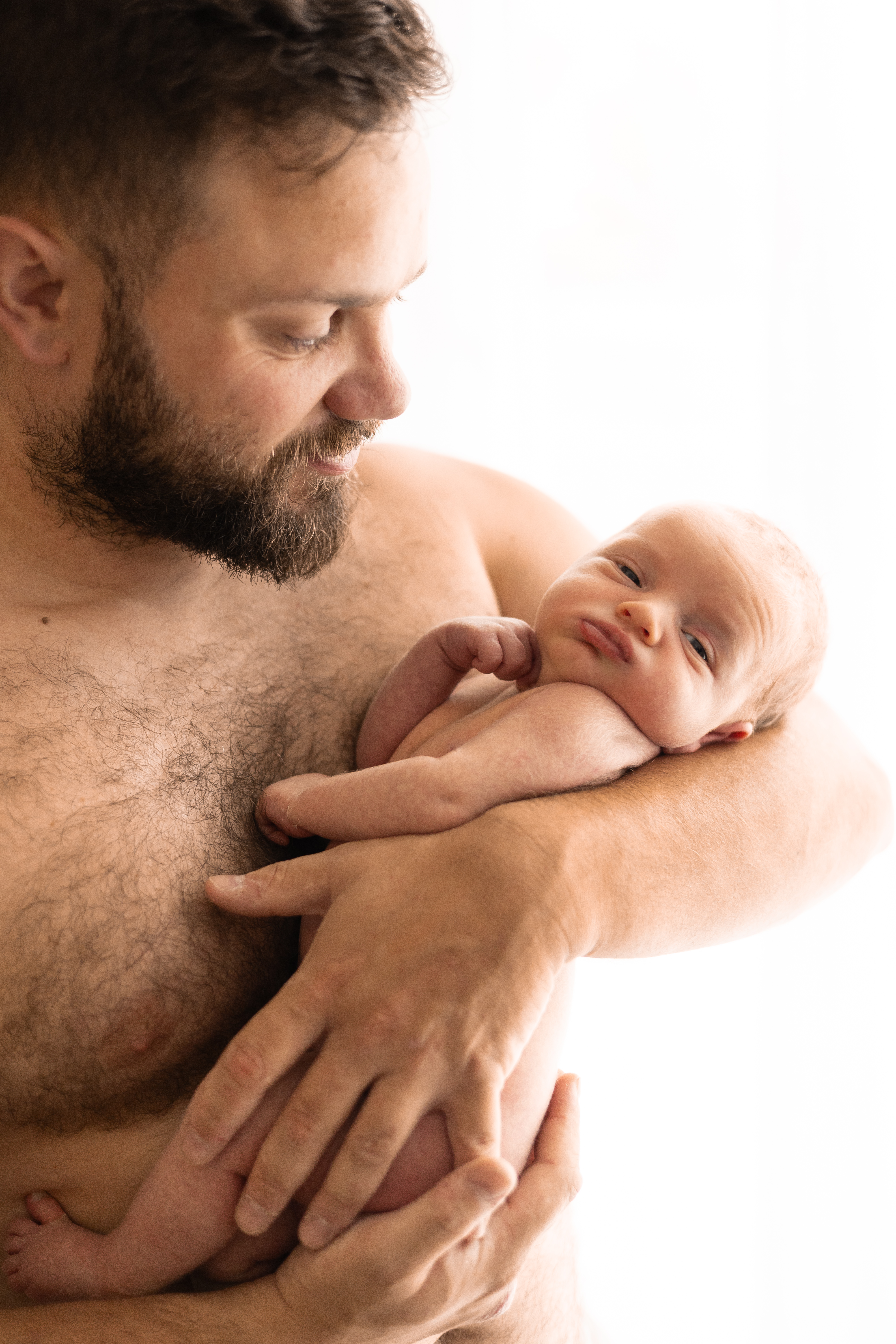 Père barbu berçant son nouveau-né souriant contre son torse