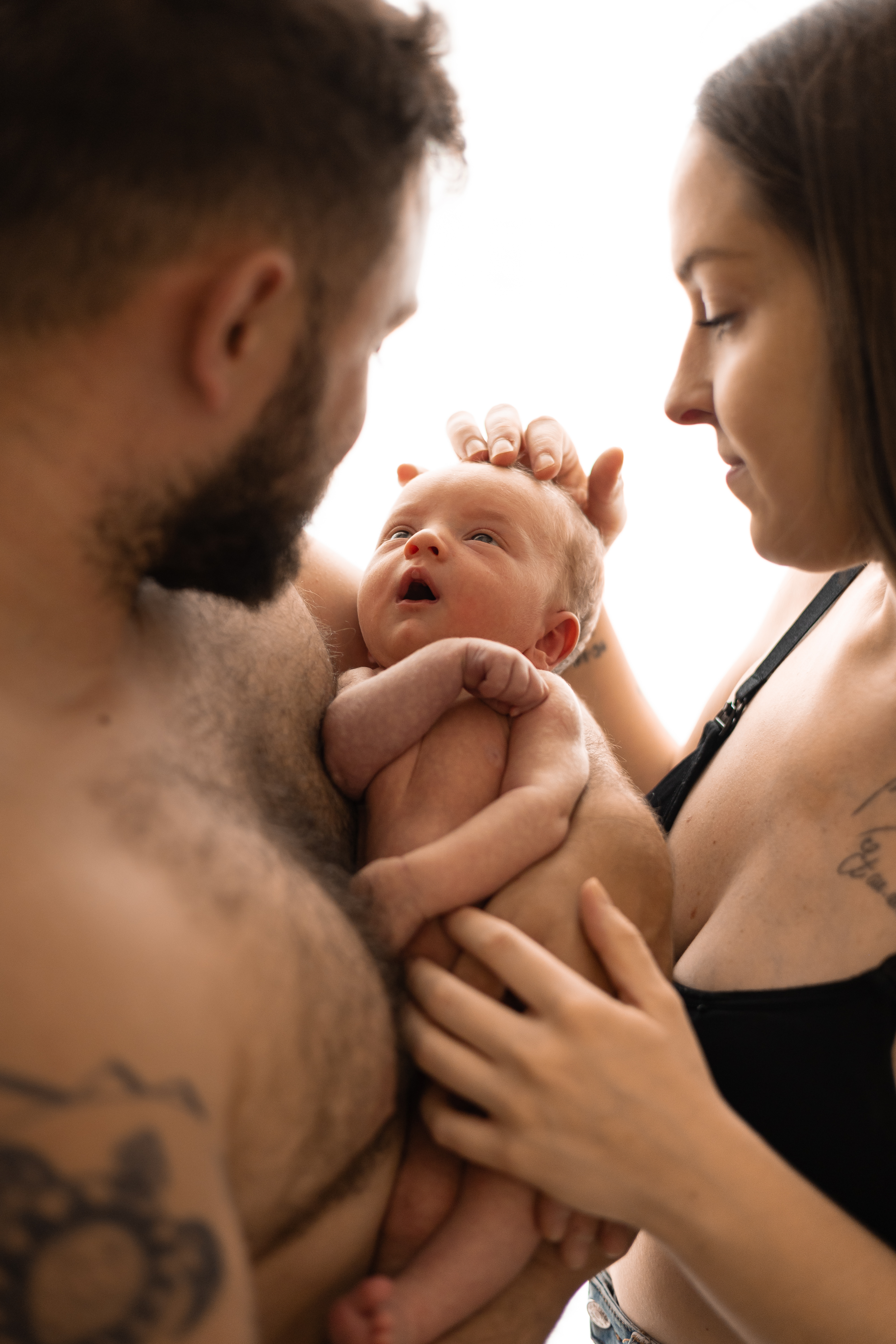 Jeunes parents contemplant leur nouveau-né tenu entre leurs visages
