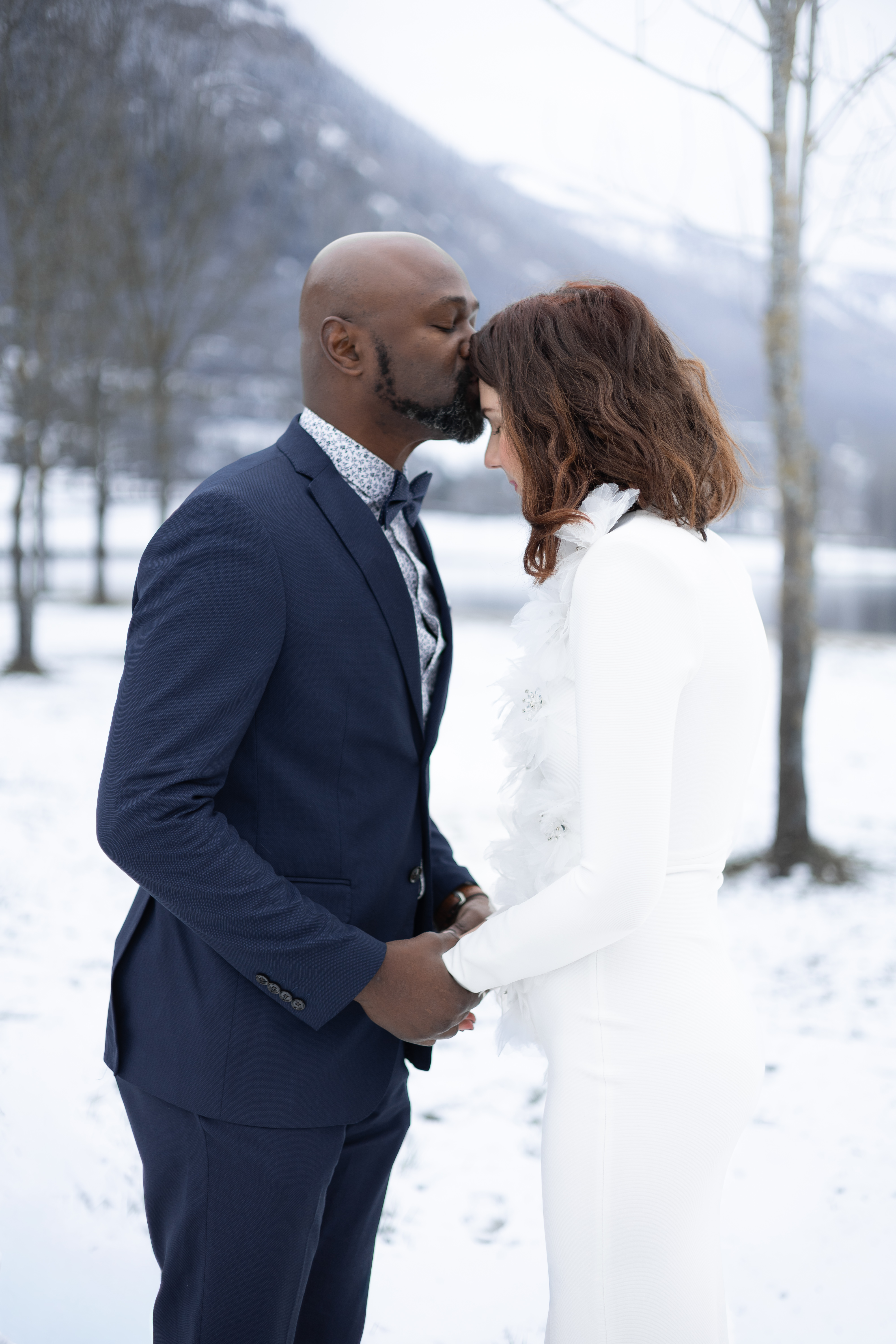 Marié déposant un baiser sur le front de son épouse dans la neige