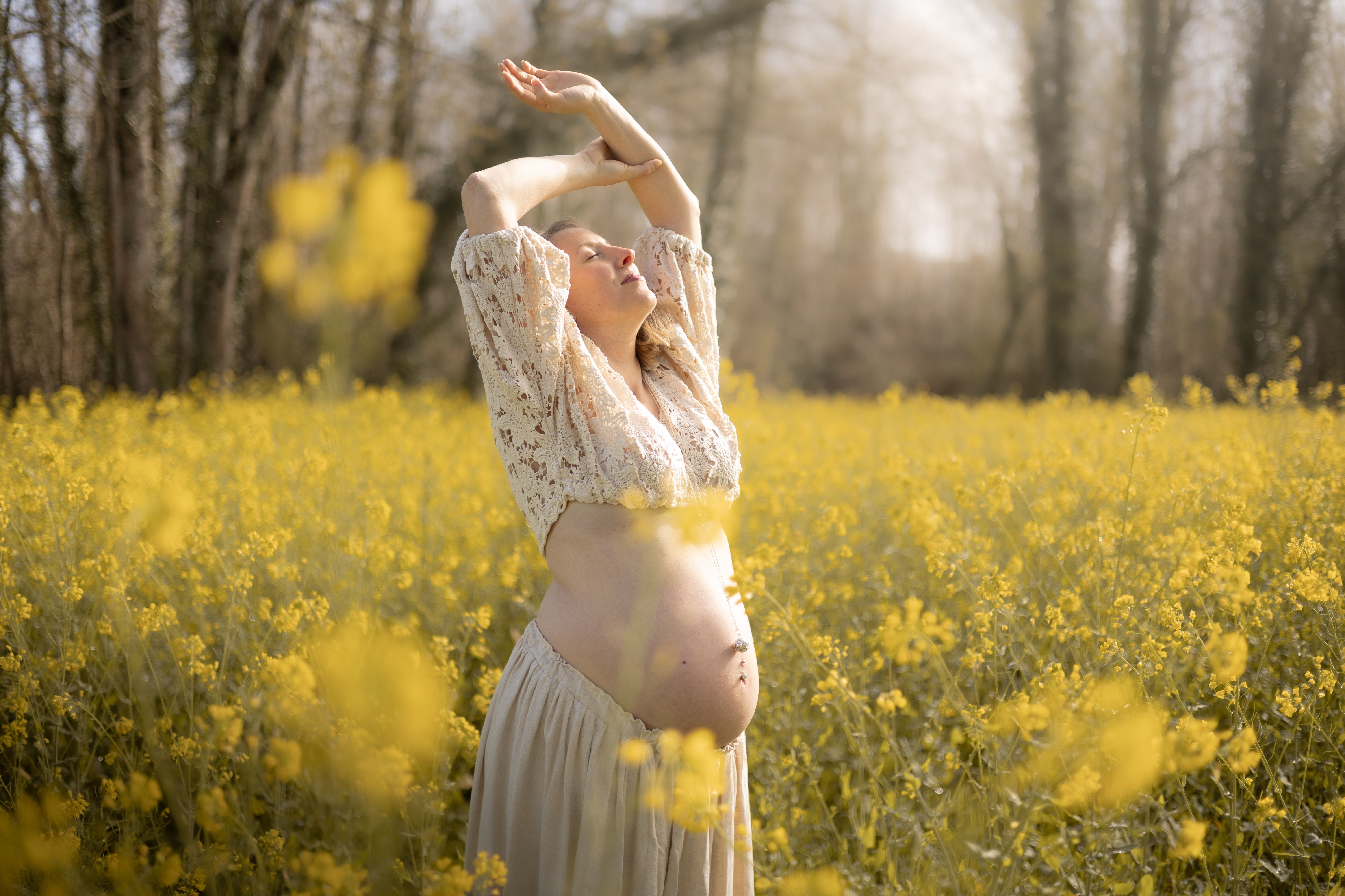Silhouette de future maman les bras levés parmi les fleurs jaunes
