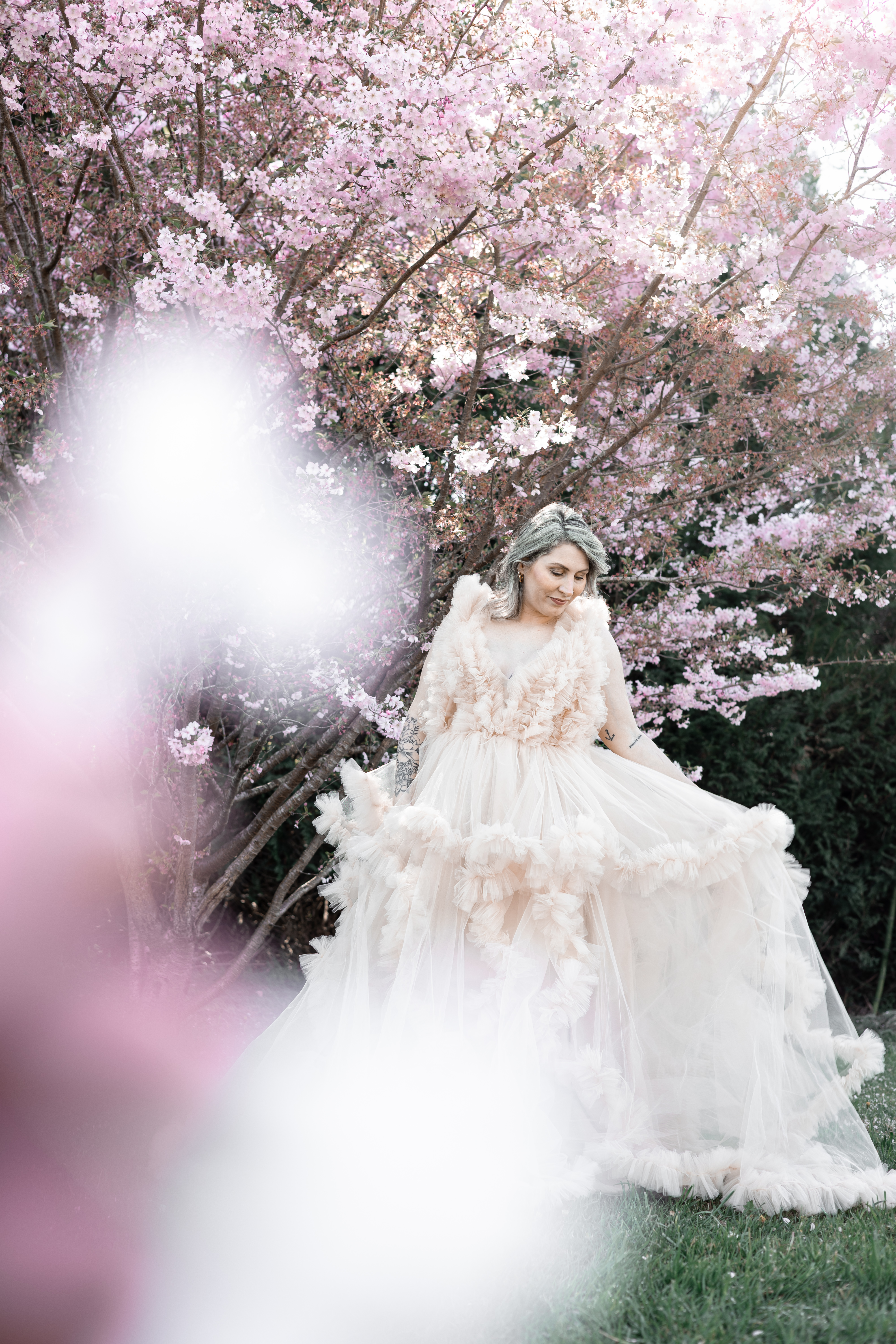 Femme en longue robe claire posant seule sous les cerisiers en fleurs