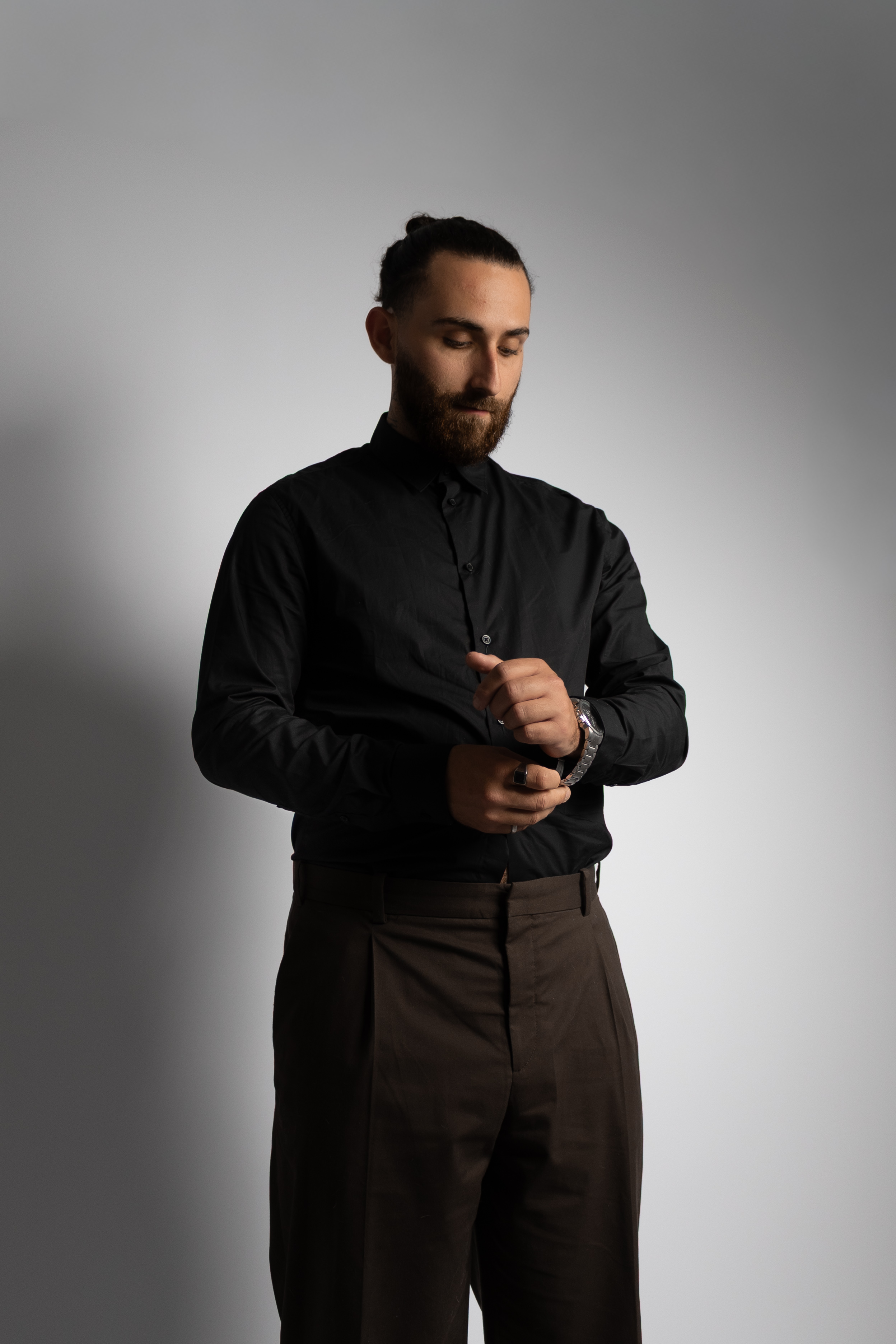 Homme en chemise noire ajustant son poignet sous une lumière latérale