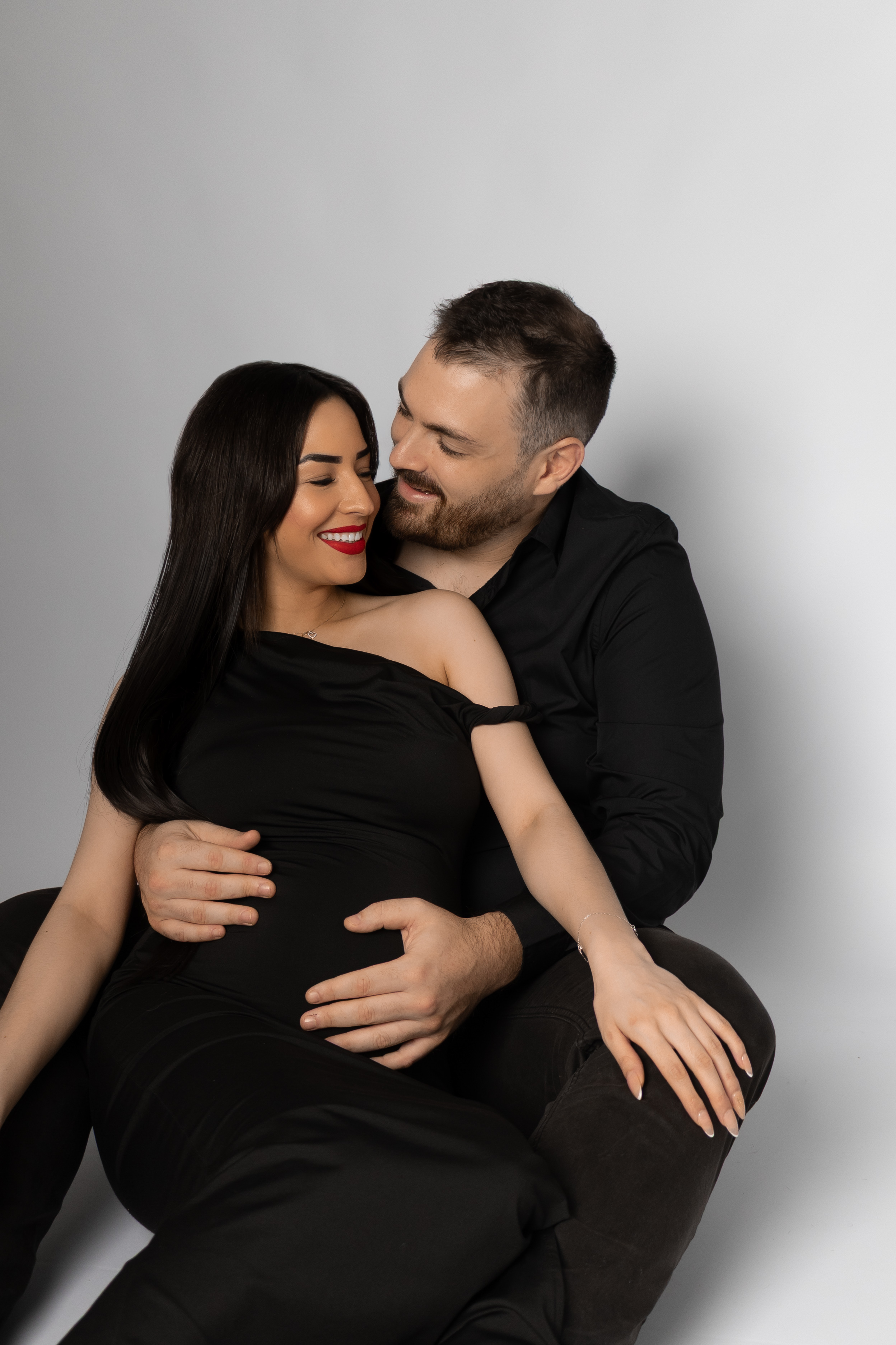 Futurs parents assis et souriants en tenues noires assorties